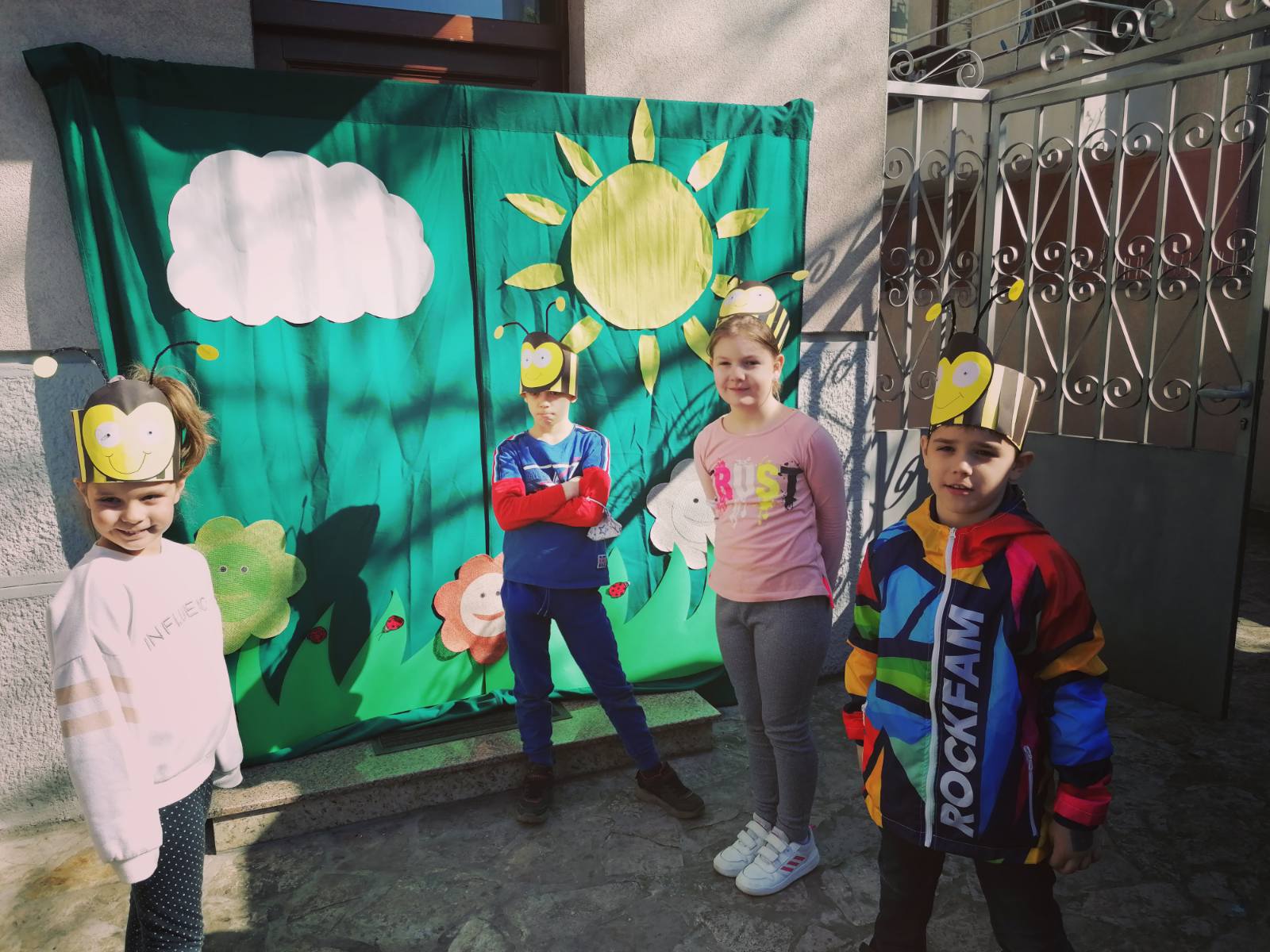 Deca maskirana u pčelice na improvizovanoj pozornici koja oslikava livadu, drveće i cveće